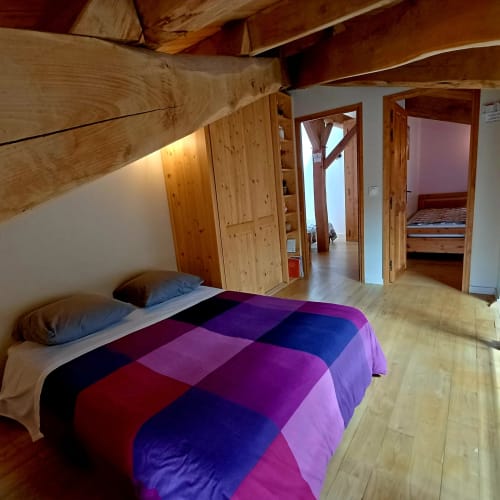 Spacieuse chambre des Gîtes Du Couvent avec courtepointe patchwork colorée, poutres apparentes et portes en bois