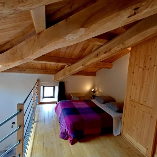 Chambre mansardée aux poutres apparentes, literie violette et petite fenêtre au Gîte 3, Les Gîtes Du Couvent, Ardèche