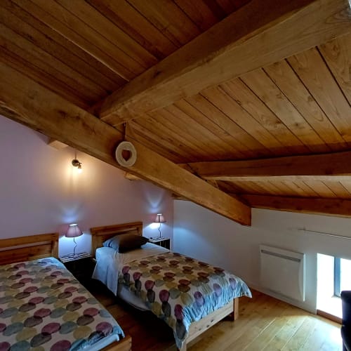 Chambre au charme rustique avec poutres apparentes, deux lits jumeaux à literie fleurie et vue sur les montagnes aux Gîtes Du Couvent