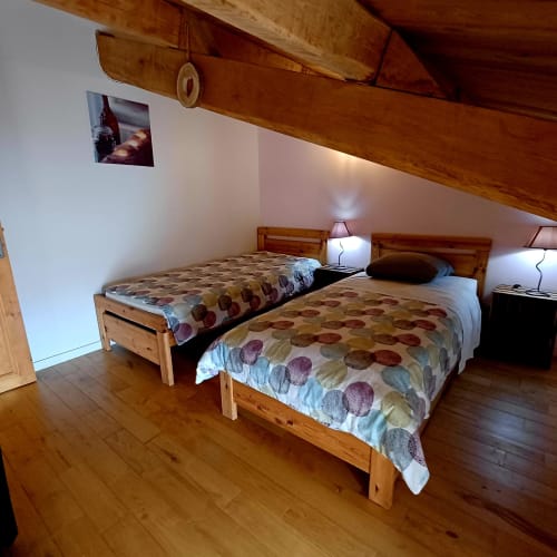 Chambre douillette sous les combles avec deux lits jumeaux en bois, couettes à motifs et lampes de chevet aux Gîtes Du Couvent, Ardèche