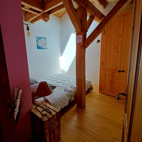 Chambre rustique aux poutres en bois, murs rose pâle, lit et porte en bois aux Gîtes Du Couvent en Ardèche.