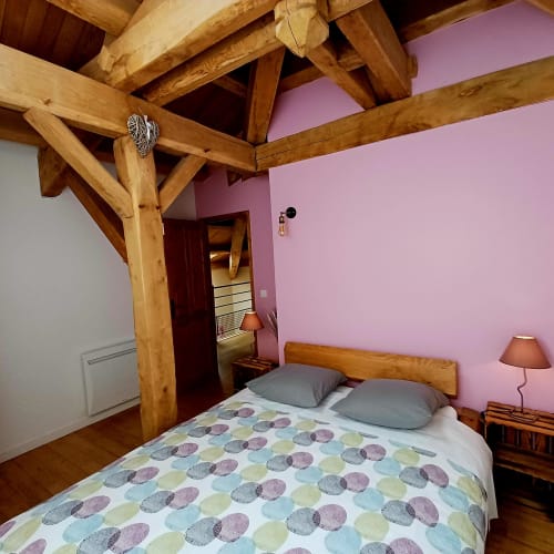 Chambre douillette aux poutres apparentes, murs roses, linge de lit motifs et lit rustique aux Gîtes Du