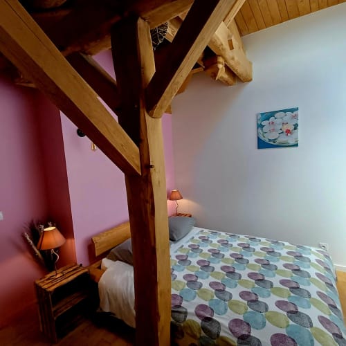Chambre douillette avec poutres apparentes, mur rose, couvre-lit patterné et mobilier rustique aux Gîtes Du Couvent