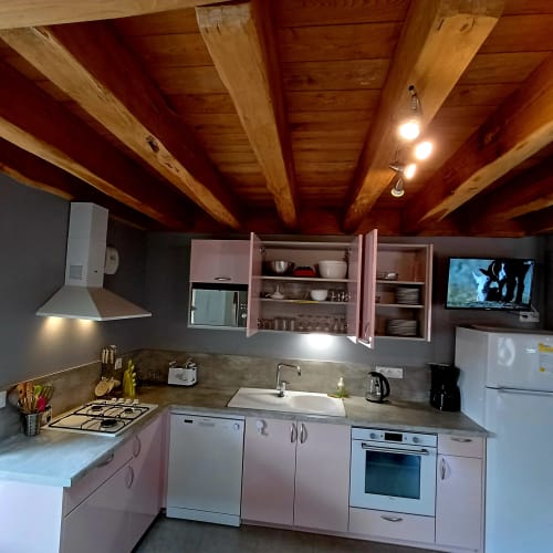 Cuisine rose moderne avec poutres apparentes, appareils inox et rangements ouverts au Gîte 3 des Gîtes