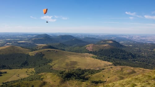 Parapentiste survolant les montagnes volcaniques verdoyantes des Trois Volcans près de Clermont-Ferrand
