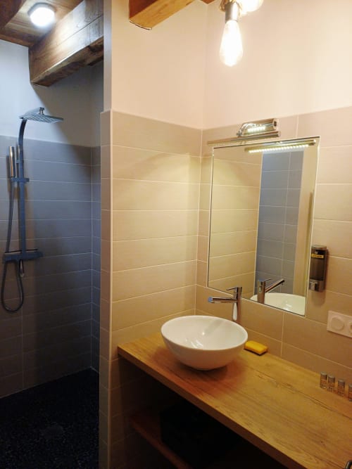Salle de bain moderne avec lavabo blanc rond, meuble en bois, miroir et douche à l'italienne aux Gîtes Du Couvent en Ardèche