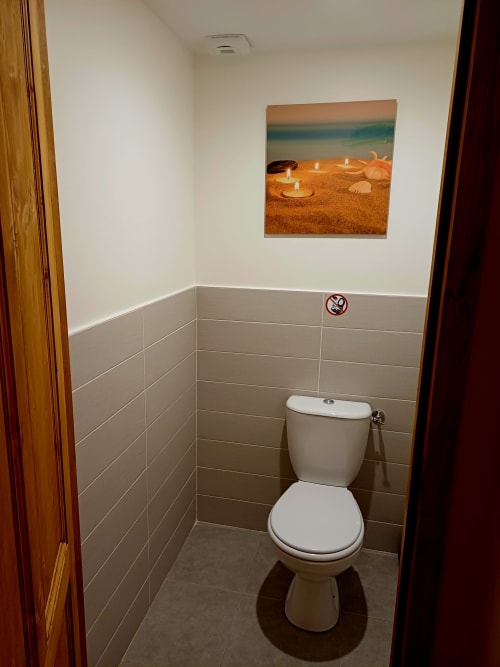 Toilettes modernes dans la salle de bains carrelée beige des Gîtes Du Couvent, Ardèche, avec décoration murale thème côtier