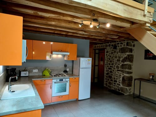 Cuisine contemporaine avec armoires orange, murs de pierre et poutres bois à la Gîte 4 des Gîtes Du Couvent, Ardèche