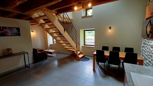 Séjour moderne aménagé ouvert avec escalier en bois, table à manger, coin lounge et baies vitrées aux Gîtes Du Couvent