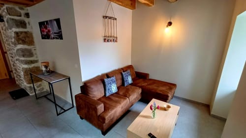 Séjour douillet avec canapé marron, poutres en bois et murs en pierre blanche aux Gîtes Du Couvent en Ardèche