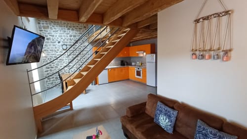 Séjour moderne aux Gîtes Du Couvent avec escalier en bois, cuisine orange, canapé marron et télévision écran plat