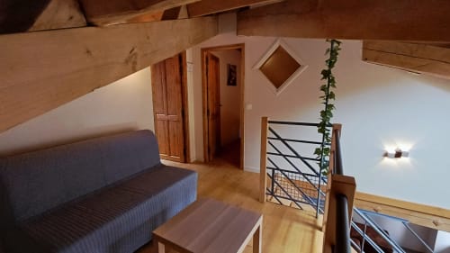 Spacieux séjour de style loft aux Gîtes Du Couvent avec canapé gris, poutres en bois et escalier orné d'un lierre