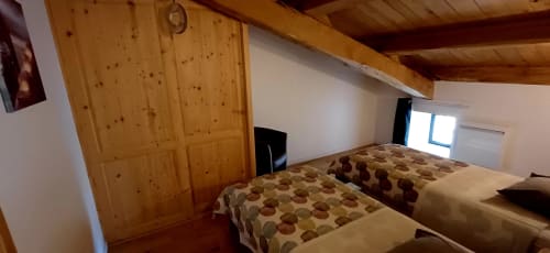 Chambre lumineuse aux Gîtes Du Couvent avec deux lits, armoire en bois, télévision et poutres apparentes en Ardèche