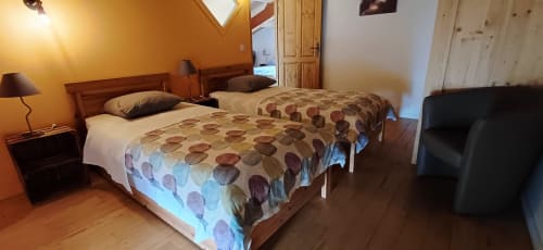 Deux lits jumeaux aux couettes à motifs dans une chambre de gîte aux Gîtes Du Couvent, Ardèche, avec mobilier en bois et ambiance chaleureuse