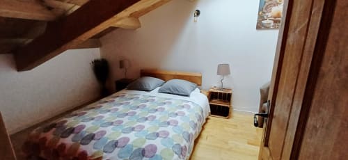 Chambre cosy aux Gîtes Du Couvent, Nozières : poutres bois, lit queen-size, lampe de chevet, parquet.