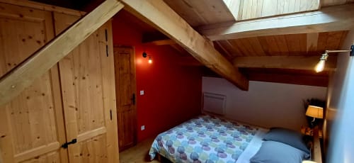 Chambre sous les toits douillette dans un gîte ardéchois : murs rouges, poutres bois, literie motifs et lucarne
