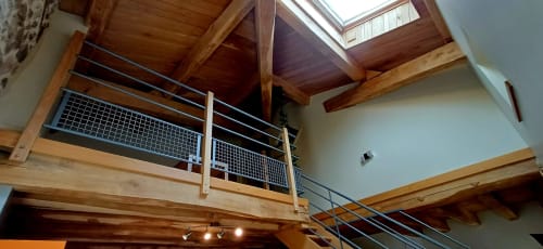 Intérieur de loft moderne aux Gîtes Du Couvent avec poutres en bois, rampes métalliques et puits de lumière en Ardèche