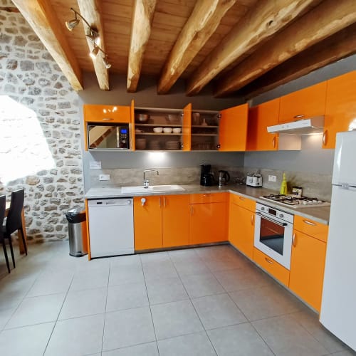 Cuisine moderne orange avec poutres en bois apparent aux Gîtes Du Couvent en Ardèche, France