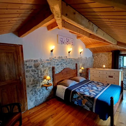 Chambre rustique aux Gîtes Du Couvent avec poutres en bois, murs en pierre, lit en bois et éclairage chaleureux en Ardèche.