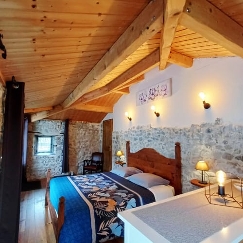 Spacieuse chambre familiale aux Gîtes Du Couvent avec poutres apparentes, lit en bois, murs de pierre et vue sur le jardin en Ardèche
