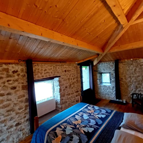 Chambre rustique en pierre avec poutres bois, literie à motifs bleus et fenêtres aux Gîtes Du Couvent