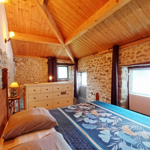 Chambre familiale spacieuse aux Gîtes Du Couvent avec plafond à poutres en bois, murs en pierre, lit queen avec couette à motifs bleus