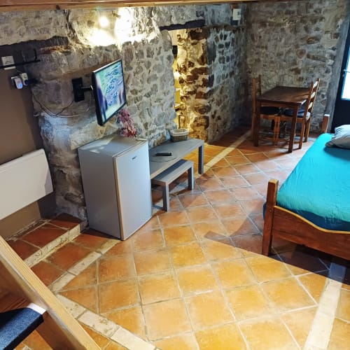 Séjour aux Gîtes Du Couvent en Ardèche : murs en pierre, carrelage en terre cuite, TV, réfrigérateur, lit et coin repas