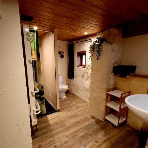 Salle de bain moderne avec douche, toilettes, baignoire et éléments en bois aux Gîtes Du Couvent, Ardèche