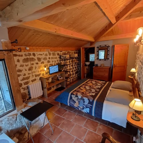 Chambre double rustique aux Gîtes Du Couvent avec pierres apparentes, poutres en bois et carrelage en terre cuite en Ardèche