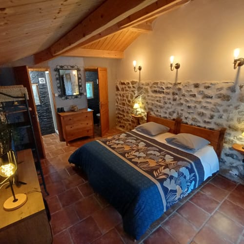 Chambre cosy aux poutres en bois, murs de pierre, literie bleue à motifs, mobilier en bois et éclairage chaleureux aux Gîtes Du