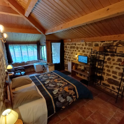 Chambre spacieuse en pierre aux Gîtes Du Couvent avec poutres apparentes, lit queen-size, vue sur jardin, TV et décor rustique en Ardèche