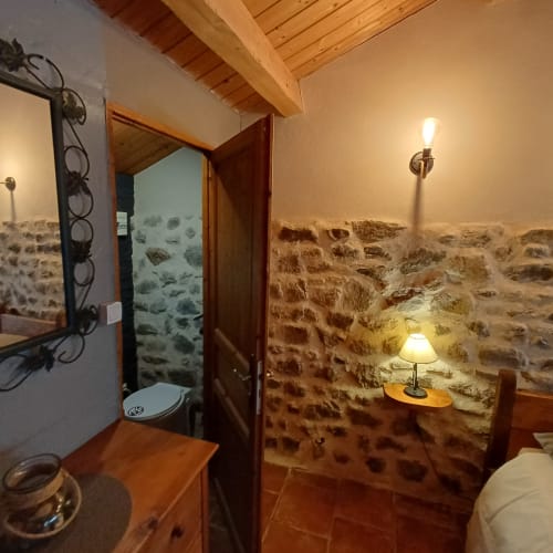 Chambre rustique en pierre aux Gîtes Du Couvent, Ardèche, avec murs apparents, poutres en bois et éclairage chaleureux