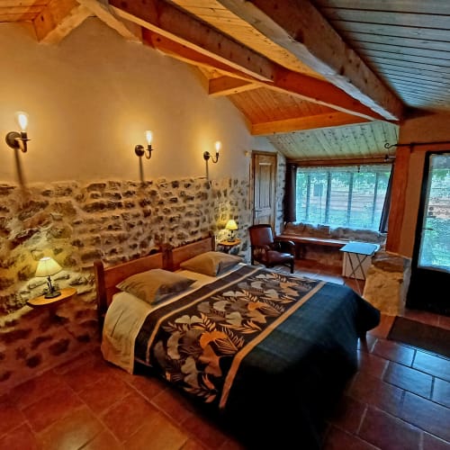 Chambre rustique en pierre aux Gîtes Du Couvent avec poutres apparentes, vue sur jardin et décor traditionnel en Ardèche, France