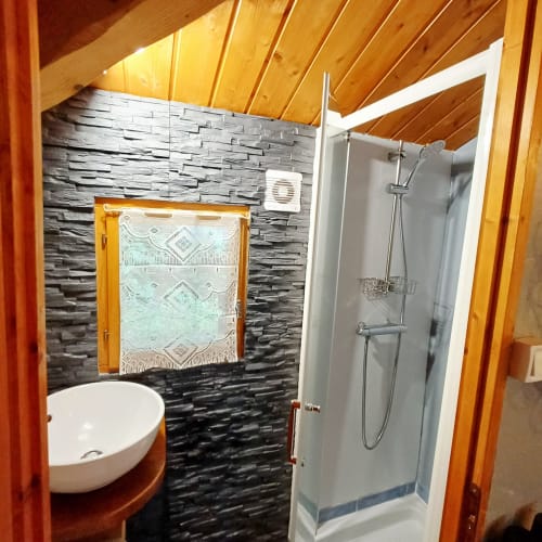 Salle de bain moderne avec murs en pierre, lavabo blanc et douche aux Gîtes Du Couvent, Ardèche