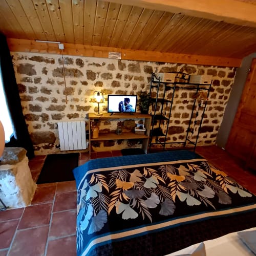 Chambre double confortable aux murs en pierre, plafond en bois, TV écran plat, literie décorée et mobilier rustique aux Gîtes