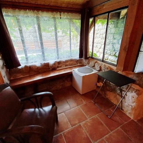 Chambre rustique aux Gîtes Du Couvent avec sol en terre cuite, banquette près de la fenêtre donnant sur le jardin et mobilier simple en Ardèche