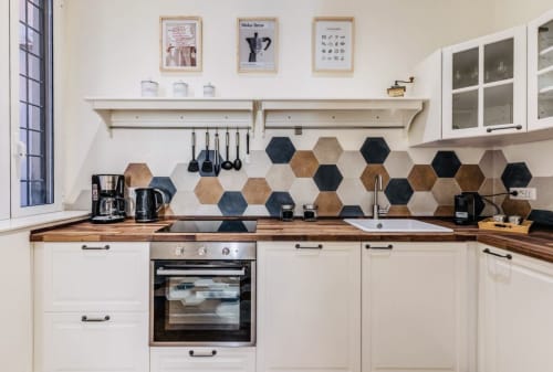 Cucina moderna dell'appartamento Rome to You con backsplash di piastrelle esagonali, banconi in legno, armadi bianchi e macchina per il caffè