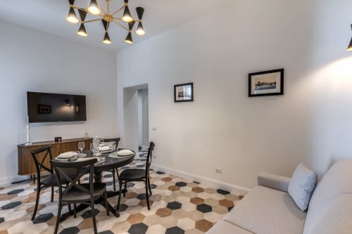 Moderna sala da pranzo nell'appartamento Rome to You con tavolo rotondo nero, elegante lampadario, TV e pavimento geometrico a Monte