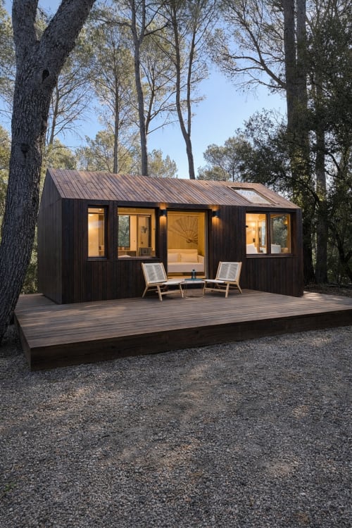 Élégante maison forestière noire au Domaine d'Olga à Aniane, illuminée chaleureusement, avec terrasse et transats