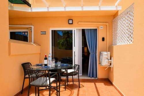 Luminosa terraza de comedor naranja en Smart Rent Fuerteventura con mesa, sillas y vistas al jardín en Tarajalejo