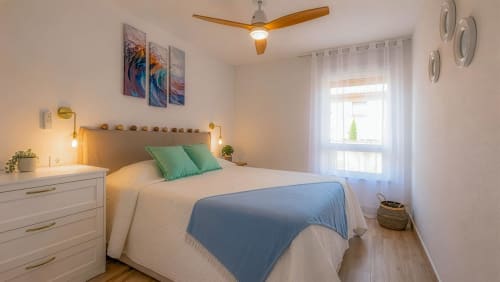 Dormitorio luminoso en Smart Rent Fuerteventura con cama queen, cojines verdes, ventilador de techo de madera y vistas al jardín