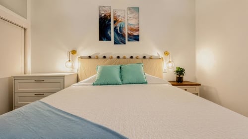 Dormitorio luminoso en apartamento Auramar, Smart Rent Fuerteventura, con cojines turquesas, lámparas colgantes e inspiración costera