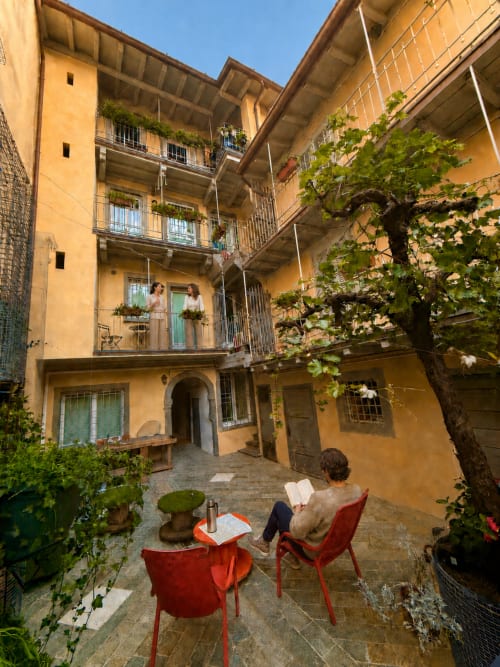Charmanter Innenhof der Bergamo-Apartments mit ockerfarbenen Gebäuden, efeu-bewachsenen Mauern und Gästen auf roten Stühlen