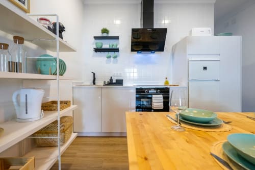 Cocina moderna en apartamento de Nerja con muebles blancos, mesa de comedor de madera y vajilla turquesa