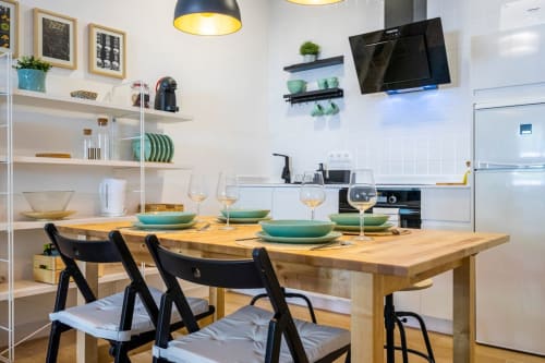 Moderna cocina-comedor en apartamento de Nerja con mesa de madera, sillas negras, vajilla turquesa y muebles blancos