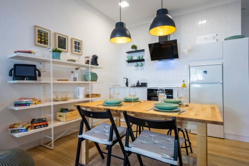Cocina moderna de apartamento en Nerja con mesa comedor, lámparas colgantes negras, estantería blanca y electrodomésticos de acero inoxidable