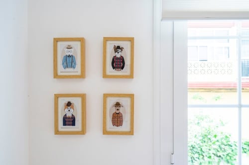 Cuatro ilustraciones enmarcadas de personajes animales en marcos de madera en pared blanca junto a ventana en apartamento de Nerja