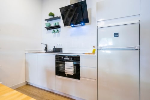 Cocina moderna en apartamento de Nerja con muebles blancos, electrodomésticos de acero inoxidable, TV montada y estanterías abiertas