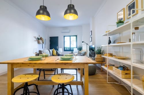 Comedor moderno del apartamento Nerja con mesa de madera, lámparas colgantes amarillas y estantería abierta en cocina contemporánea luminosa