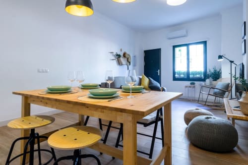 Zona de comedor moderna en apartamento de Nerja con mesa de madera, platos verdes e iluminación colgante con vistas al salón